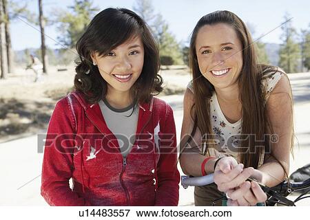 Stock Photo - Two young women standing outdoors with mountain bike, portrait.. Fotosearch