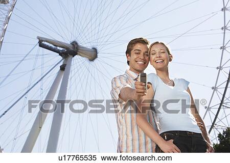 Vacationing Couple Photographing Themselves with mobile phone by London Eye View Large Photo Image Stock Photography - Vacationing Couple Photographing Themselves with mobile phone by London Eye. Fotosearch