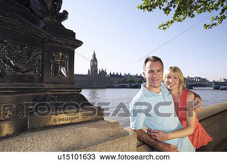 Stock Image - Vacationing couple standing by Thames River, portrait. Fotosearch