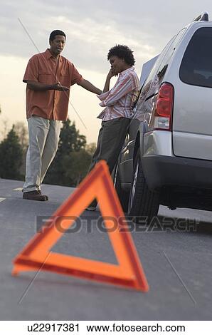 Stock Image - Warning triangle in front of broken down car, people in background. Fotosearch