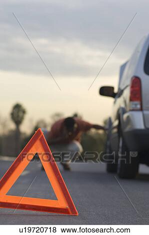 Stock Photo - Warning triangle in front of broken down car, man in background. Fotosearch