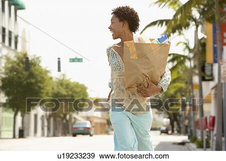 Stock Photo - Woman carrying grocery bag while walking, profile. Fotosearch