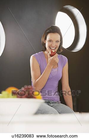 Woman eating apple, sitting on kitchen surface View Large Photo Image Stock Image - Woman eating apple, sitting on kitchen surface. Fotosearch