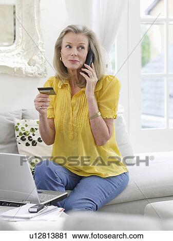 Woman holding credit card using phone in living room View Large Photo Image Stock Image - Woman holding credit card using phone in living room. Fotosearch