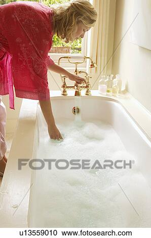 Woman in bathrobe bending down over bathtub filled with bubbles, testing water, side view View Large Photo Image Stock Image - Woman in bathrobe bending down over bathtub filled with bubbles, testing water, side view. Fotosearch