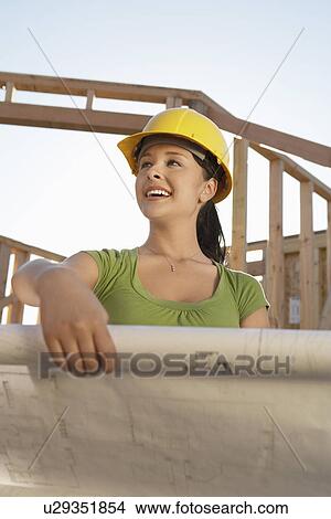 Picture - Woman in hard hat on building site with blue prints. Fotosearch