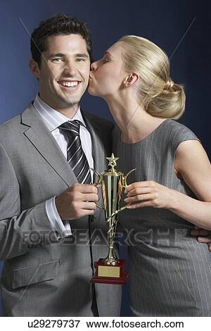 Woman kissing man holding trophy against dark background View Large Photo Image Stock Photo - Woman kissing man holding trophy against dark background. Fotosearch