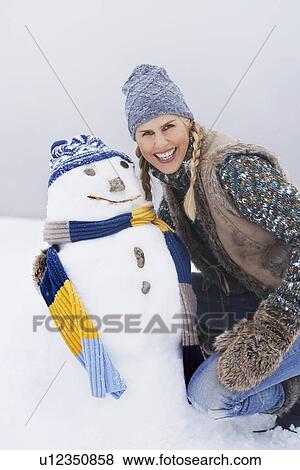Woman kneeling by snowman on snow-covered hill View Large Photo Image Stock Photo - Woman kneeling by snowman on snow-covered hill. Fotosearch