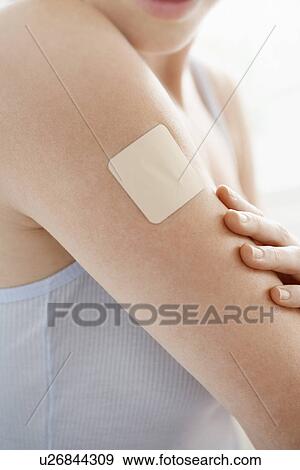 Stock Photo - Woman looking at nicotine patch on arm, mid-section, close up. Fotosearch