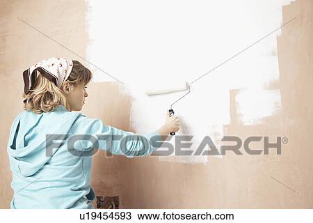 Stock Image - Woman painting interior wall with paint roller. Fotosearch