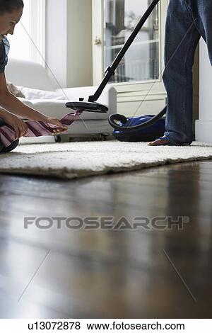 Stock Photo - Woman pulling tie from vacuum cleaner in bedroom. Fotosearch