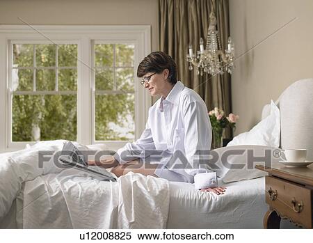 Stock Photography - Woman reading newspaper in bed. Fotosearch