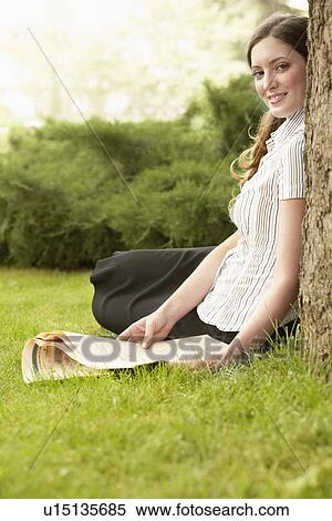 Stock Photography - Woman sitting on grass holding newspaper, side view portrait.. Fotosearch