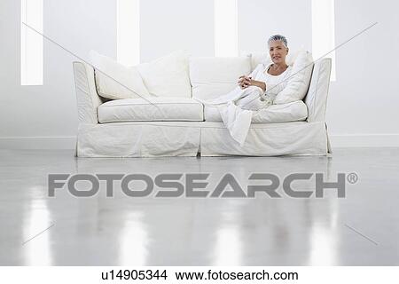 Picture - Woman sitting on sofa in empty white room, portrait. Fotosearch