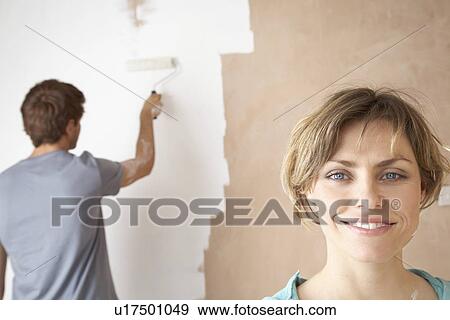 Stock Photo - Woman smiling while man roller paints interior wall. Fotosearch