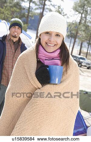 Picture - Woman stands in campsite wrapped in blanket and holding cup. Fotosearch