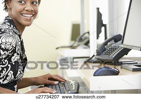 Stock Photo - Woman using computer in office, smiling. Fotosearch