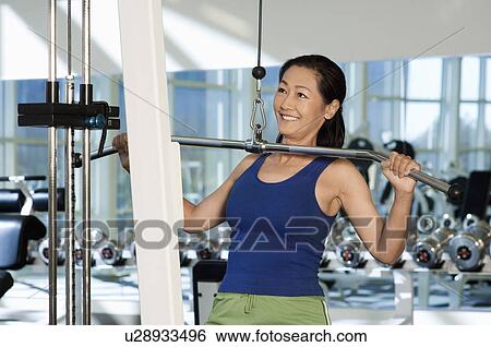 Stock Photograph - Woman using exercise equipment in gymnasium. Fotosearch