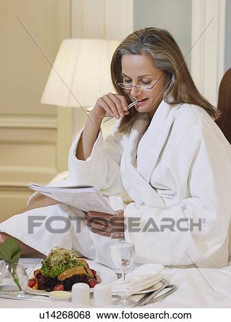 Stock Photo - Woman wearing bathrobe sitting on bed reading. Fotosearch