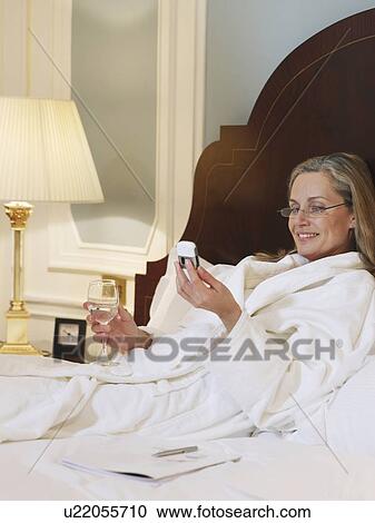 Stock Image - Woman wearing bathrobe using mobile phone, lying on bed. Fotosearch
