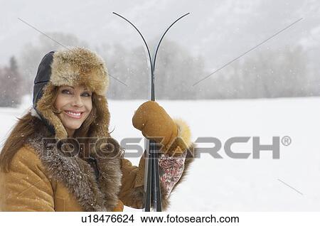 Picture - Woman wearing fur coat and hat, holding skis, in snow covered field, portrait.. Fotosearch