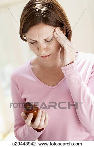 Stock Image - Woman with headache holding pills, touching head. Fotosearch