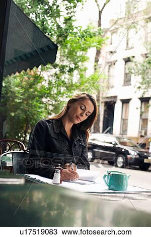 Stock Image - Woman writing at sidewalk cafe. Fotosearch