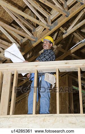 Stock Image - Worker holding blueprint in construction site. Fotosearch