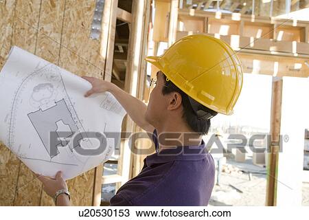 Stock Image - Worker holding blueprint in construction site. Fotosearch