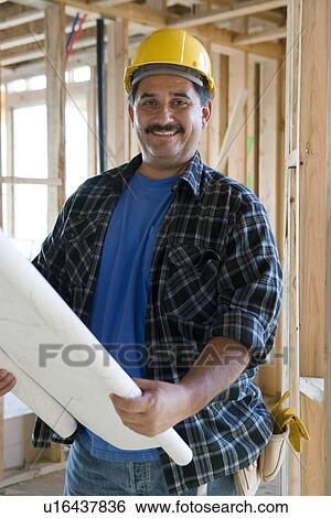 Stock Photograph - Worker holding blueprint in construction site. Fotosearch