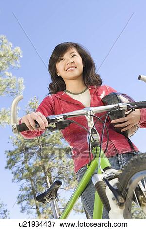 Stock Photo - Young Asian woman stands with cycling helmet and mountain bike. Fotosearch