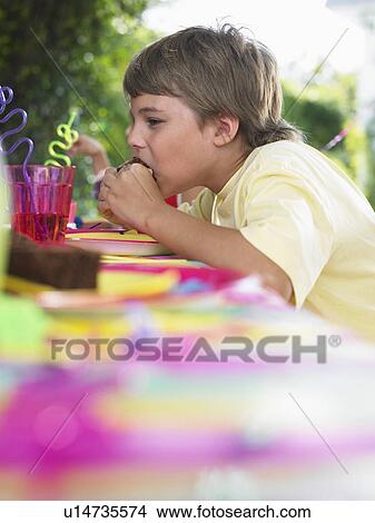 Young boy (10-12) eating cupcake at birthday party View Large Photo Image Picture - Young boy (10-12) eating cupcake at birthday party. Fotosearch