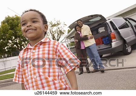 Stock Photo - Young boy standing in front of parents by car. Fotosearch
