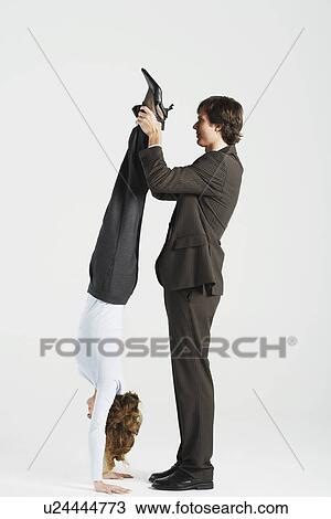 Stock Image - Young businessman holding legs of female colleague standing on hands, profile. Fotosearch