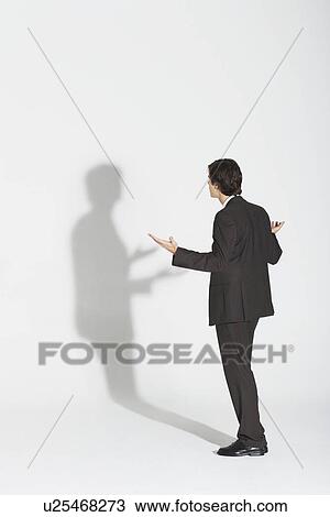 Young businessman standing, arguing with own shadow View Large Photo Image Stock Image - Young businessman standing, arguing with own shadow. Fotosearch