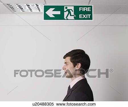 Stock Photography - Young businessman standing under exit sign. Fotosearch