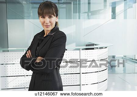 Stock Photo - Young businesswoman standing in office corridor, smiling, portrait. Fotosearch