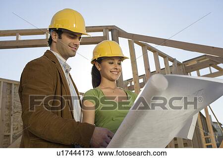 Young couple examining blueprint in construction site View Large Photo Image Stock Image - Young couple examining blueprint in construction site. Fotosearch