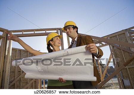 Young couple examining blueprint in construction site View Large Photo Image Stock Photo - Young couple examining blueprint in construction site. Fotosearch