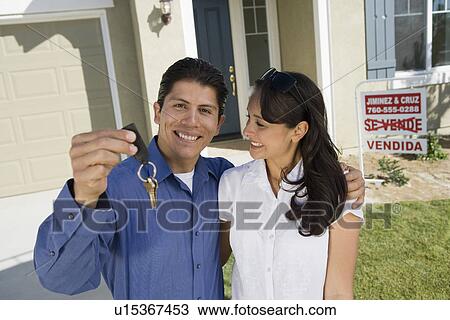 Stock Image - Young couple holding keys outside new home, portrait. Fotosearch