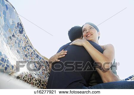 Young couple hugging on stone bench, portrait, low angle view View Large Photo Image Stock Image - Young couple hugging on stone bench, portrait, low angle view. Fotosearch