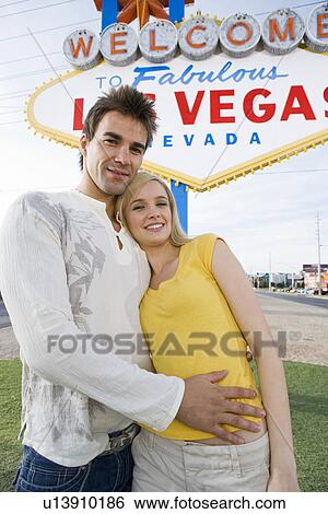 Stock Photograph - Young couple in front of Welcome to Las Vegas sign, portrait. Fotosearch