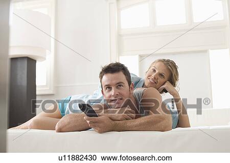 Stock Image - Young couple lying on bed and watching TV. Fotosearch