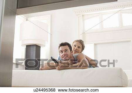 Young couple lying on bed and watching TV View Large Photo Image Stock Photo - Young couple lying on bed and watching TV. Fotosearch