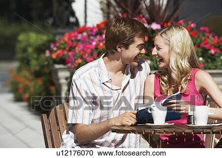 Young couple sitting at outdoor cafe laughing and holding guidebook View Large Photo Image Stock Image - Young couple sitting at outdoor cafe laughing and holding guidebook. Fotosearch