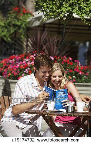 Young couple sitting at outdoor cafe laughing and holding guidebook View Large Photo Image Stock Image - Young couple sitting at outdoor cafe laughing and holding guidebook. Fotosearch