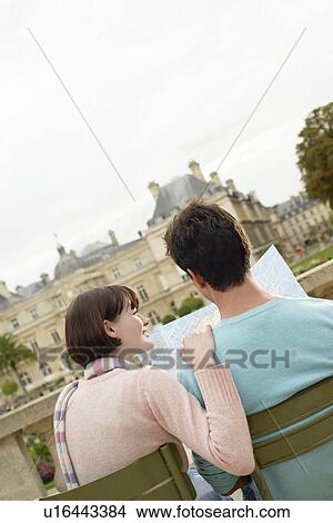 Picture - Young couple sitting on chairs, looking at map, in park, back view. Fotosearch