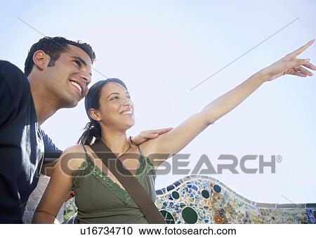 Young couple sitting on stone bench, woman pointing into distance, portrait View Large Photo Image Stock Image - Young couple sitting on stone bench, woman pointing into distance, portrait. Fotosearch