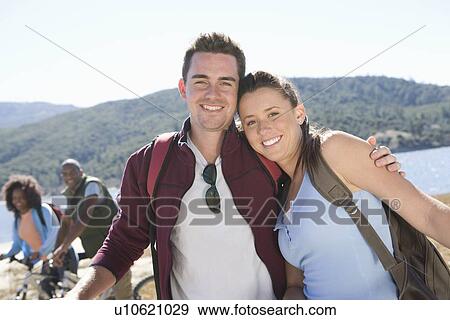 Young couple stand at lakeside, man with his arm around the woman View Large Photo Image Stock Photo - Young couple stand at lakeside, man with his arm around the woman. Fotosearch