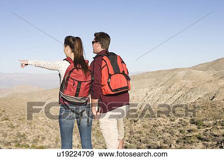 Stock Photo - Young couple stand looking at view, woman points. Fotosearch